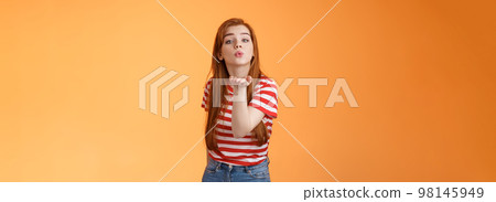 Silly cute and flirty redhead passionate girl, send air kiss camera, fold lips hold arm near mouth to blow mwah, romantic tender attitude, confess love like guy, stand orange background Silly cute and flirty redhead passionate girl, send air kiss camera, fold lips hold arm near mouth to blow mwah, romantic tender attitude, confess love like guy, stand orange background 98145949
