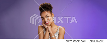 Tender elegant wealthy young african american rich woman in brilliants silver stylish shiny dress lean head shoulder smiling flirty romantic gaze camera standing amused blue background Tender elegant wealthy young african american rich woman in brilliants silver stylish shiny dress lean head shoulder smiling flirty romantic gaze camera standing amused blue background 98146205