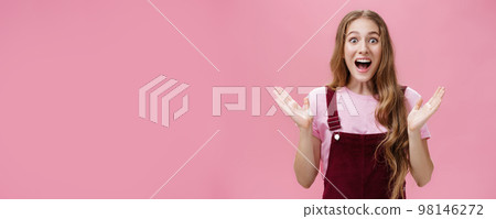 Waist-up shot of excited happy and impressed charming caucasian girlfriend in overalls and t-shirt raising hands in surprise and amazement cheering smiling broadly from astonishment over pink wall Waist-up shot of excited happy and impressed charming caucasian girlfriend in overalls and t-shirt raising hands in surprise and amazement cheering smiling broadly from astonishment over pink wall 98146272