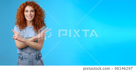 Which way. Charismatic attractive happy smiling redhead curly girl pointing curious sideways cross arms body indicating left right intrigued what choose making decision standing blue background 98146297