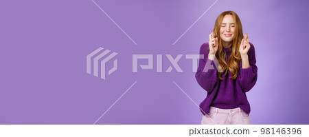 Girl makes wish eager dream come true. Atractive hopeful and positive young redhead woman in purple sweater close eyes and smiling as cross fingers for good luck, praying and anticipating miracle Girl makes wish eager dream come true. Atractive hopeful and positive young redhead woman in purple sweater close eyes and smiling as cross fingers for good luck, praying and anticipating miracle 98146396