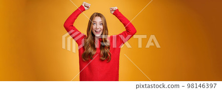 Optimistic happy and supportive ginger girl yelling cheering words, raising hands joyfully and smiling broadly triumphing, celebrating success and win, posing satisfied and excited against orange wall Optimistic happy and supportive ginger girl yelling cheering words, raising hands joyfully and smiling broadly triumphing, celebrating success and win, posing satisfied and excited against orange wall 98146397