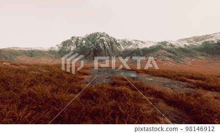 Plain with dried grass and mountain peaks in the background 98146912