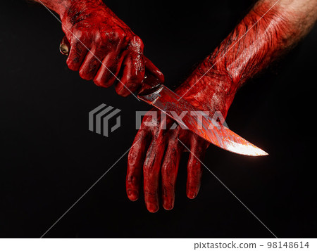 A man wipes a bloody knife with his hand on a black background.  98148614