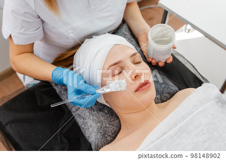 Cosmetician giving client facial skincare mask. Beautician working 98148902