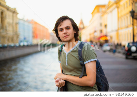 Young male man tourist with medium length hair in old city, river channel. European caucasian white man, looking at camera student, musician, violinist, painter, artist. Lifestyle portrait Young male man tourist with medium length hair in old city, river channel. European caucasian white man, looking at camera student, musician, violinist, painter, artist. Lifestyle portrait 98149160