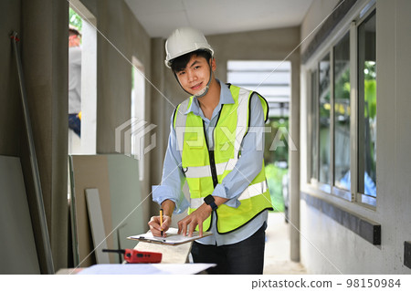 Portrait of asian male engineer in a protective helmet standing in construction site and looking at camera 98150984