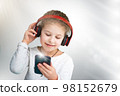 A beautiful little girl listens to music on headphones, holds a phone in her hands. generation concept 98152679