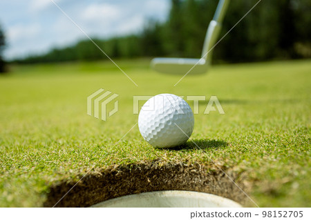 Hole on the golf course, next to a white ball Hole on the golf course, next to a white ball 98152705