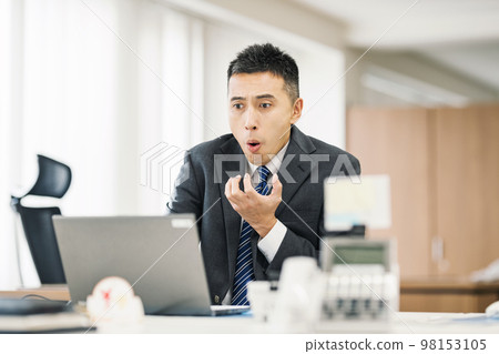 Surprised businessman looking at the computer screen Surprised businessman looking at the computer screen 98153105