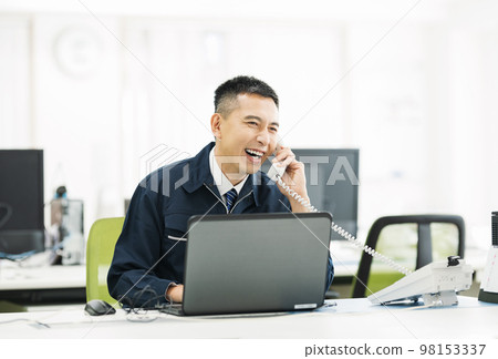 A man in work clothes answering the phone in the office 98153337