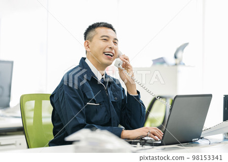 一個穿著工作服的男人在辦公室接電話 98153341