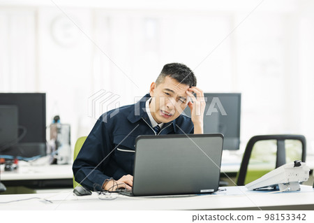 A man in work clothes who is worried while looking at a computer in the office 98153342