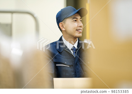一個穿著工作服的男人在配送倉庫裡提著紙箱 98153385