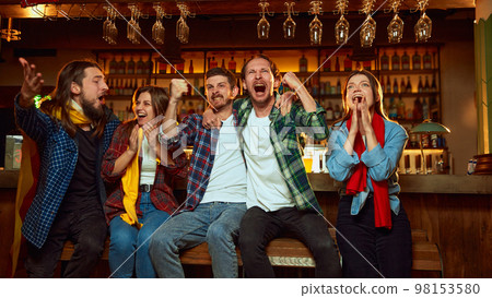 Group of young people, friends, emotionally watching match at pub. Fans cheering up favourite sport team. Winning game. Success 98153580
