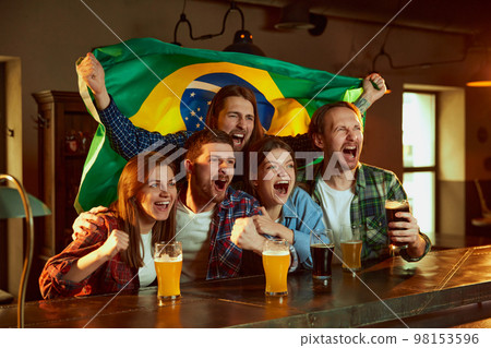 Friends,young people, men and women watching football match at pub. Fans emotionally cheering up Brazil team. Drinking beer 98153596