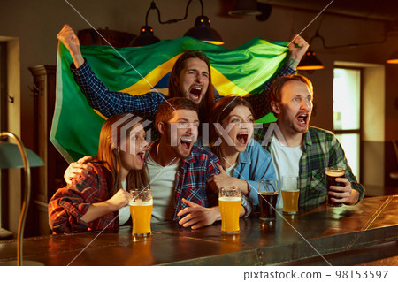 Group of young people, men and women watching football match at pub. Fans emotionally cheering up Brazil team. Friends meeting 98153597