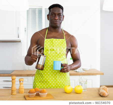 Handsome man in apron drinking coffee at home 98154070