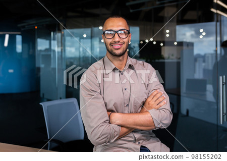 Portrait of hispanic successful businessman, successful man in shirt looking at camera with crossed arms, worker inside office near window. 98155202