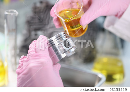 Scientist pours engine oil on piston of car in laboratory closeup 98155339