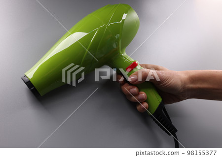Woman hands hold a green hair dryer on gray background 98155377