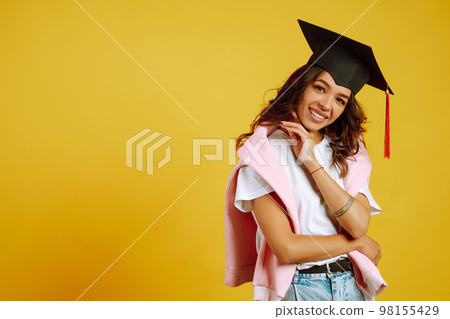 Graduate woman in graduation hat on her head posing on yellow background. Study, education, college. 98155429