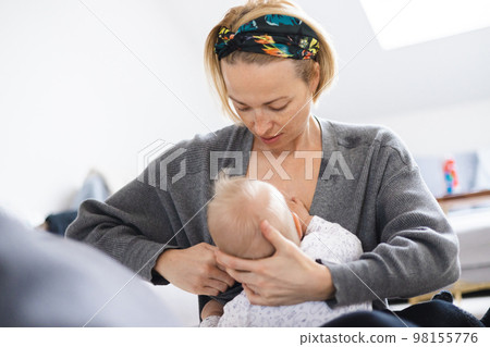 Young woman breastfeeding her infant baby boy casualy sitting on child's playing mat on living room floor at home Young woman breastfeeding her infant baby boy casualy sitting on child's playing mat on living room floor at home 98155776