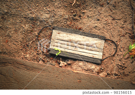 Black old dirty disposable medical mask lying on sand road near pavement Black old dirty disposable medical mask lying on sand road near pavement 98156015