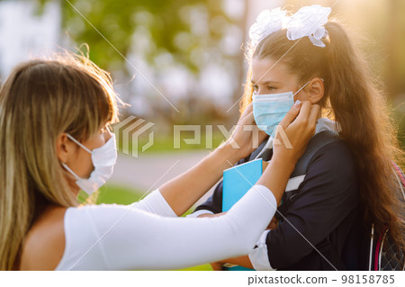 Little girl and mom in medical mask during covid-19 at sunset. Virus, pandemic, outbreak, epidemic. Little girl and mom in medical mask during covid-19 at sunset. Virus, pandemic, outbreak, epidemic. 98158785