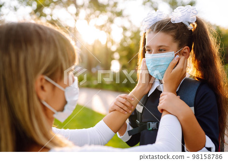 Little girl and mom in medical mask during covid-19 at sunset. Virus, pandemic, outbreak, epidemic. Little girl and mom in medical mask during covid-19 at sunset. Virus, pandemic, outbreak, epidemic. 98158786