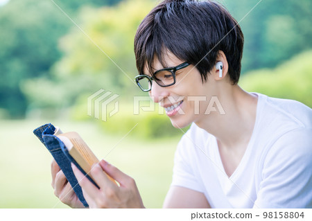 A foreign man reading while listening to music in a fresh green park A foreign man reading while listening to music in a fresh green park 98158804