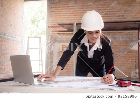 Young caucasian architect woman looking laptop and working drawing blueprint for planning. 98158990