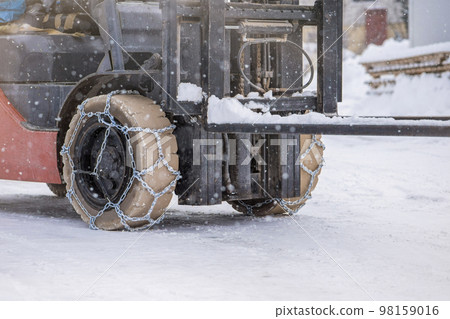 Tractor wheel with chain. Tractor or loader on a slippery snowy road. Loaders drive on snow with anti-skid chains. Tractor wheel with chain. Tractor or loader on a slippery snowy road. Loaders drive on snow with anti-skid chains. 98159016