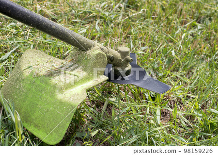 A hand-held lawn mower mows the grass in the summer in the garden. For a garden equipment store. A hand-held lawn mower mows the grass in the summer in the garden. For a garden equipment store. 98159226