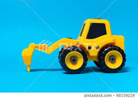 Children's toy yellow tractor truck drill on a blue background. Plastic construction equipment, toy store. Children's toy yellow tractor truck drill on a blue background. Plastic construction equipment, toy store. 98159229