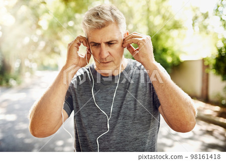 Fit, mature and healthy or sporty athlete resting after morning run, listening to music outdoors with earphones. Male jogger about to exercise or do cardio training workout for wellness lifestyle. Fit, mature and healthy or sporty athlete resting after morning run, listening to music outdoors with earphones. Male jogger about to exercise or do cardio training workout for wellness lifestyle. 98161418
