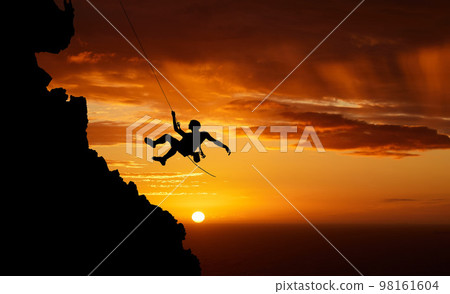 Sunset sky abseiling, mountain silhouette and hiking man hanging on shadow rope. Fitness risk, adventure freedom challenge and strong, surreal nature adrenaline and cliff climbing on orange landscape Sunset sky abseiling, mountain silhouette and hiking man hanging on shadow rope. Fitness risk, adventure freedom challenge and strong, surreal nature adrenaline and cliff climbing on orange landscape 98161604