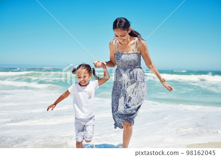 Beach, mother and girl being happy, relax and playful for summer, vacation and holding hands together. Mama, child and daughter being joyful, enjoy seaside and smile while on travel for bonding. 98162045