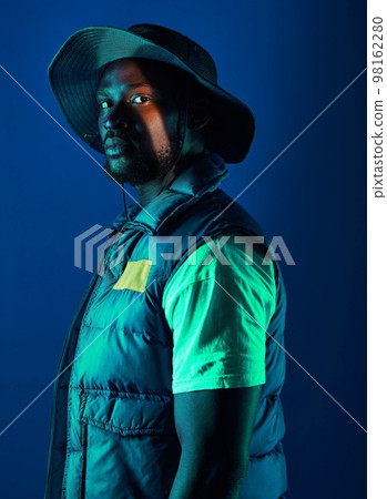 Fashion, trendy and black man model in a studio with a cool, stylish and casual outfit with lighting. Edgy, style and modern fashionable African male posing while isolated by a blue background. 98162280