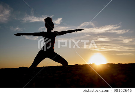 Silhouette, yoga and sunset with woman on rock for training, fitness and zen wellness. Spiritual, faith and health with pilates girl workout with warrior pose in nature for relax, peace and balance 98162646