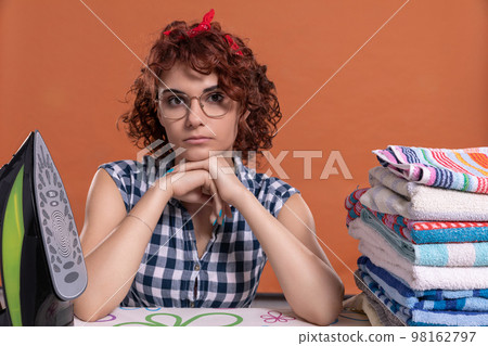 After ironing the towels, the young girl sits and looks straight into the camera. After ironing the towels, the young girl sits and looks straight into the camera. 98162797