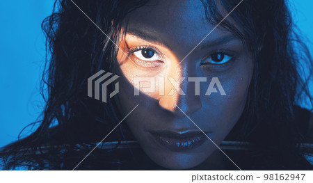 Beauty, cosmetics and portrait of a model with a light reflection on her face in the studio. Spotlight, skincare and young woman from Puerto Rico with natural skin isolated by a blue background. Beauty, cosmetics and portrait of a model with a light reflection on her face in the studio. Spotlight, skincare and young woman from Puerto Rico with natural skin isolated by a blue background. 98162947