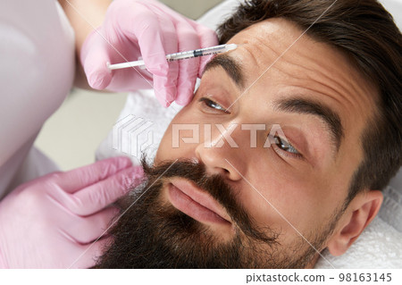 Closeup of bearded man getting beauty injection at aesthetic clinic. Doctor injecting anti-aging filler in handsome male face Closeup of bearded man getting beauty injection at aesthetic clinic. Doctor injecting anti-aging filler in handsome male face 98163145