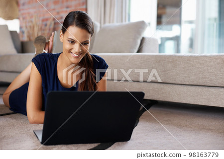 Surfing the net at home. an attractive young woman using her laptop while relaxing on the floor at home. Surfing the net at home. an attractive young woman using her laptop while relaxing on the floor at home. 98163779