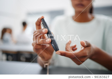 Diabetes, finger and black woman with blood sugar test on to check levels of student while sitting at desk. Healthcare, health and female prick to use glucose meter for insulin and wellness 98163827
