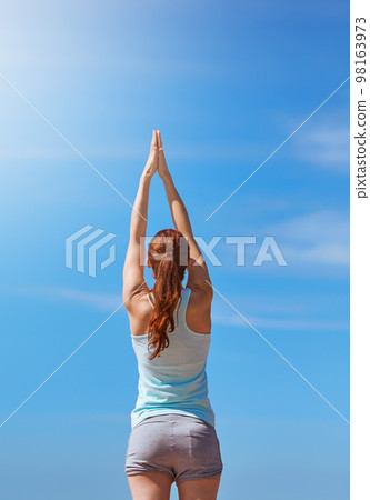 Woman, exercise and yoga for meditation with hands in air against blue sky for freedom, health and wellness outdoor. Fitness model in prayer pose for workout, mindfulness and mental health meditation 98163973