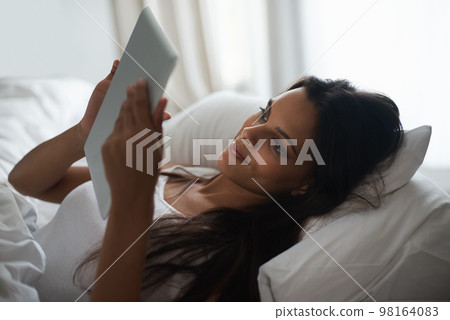 Browsing in bed. a beautiful young woman relaxing in bed with her tablet. 98164083