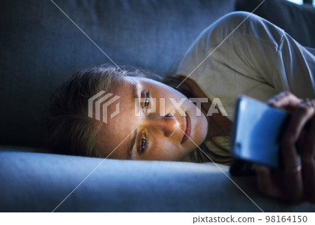 Phone, night and sad woman relaxing on sofa in living room scrolling on social media after a break up. Depression, upset and girl on couch in lounge reading student loan or debt emails on smartphone. 98164150