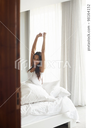 Rise and shine. An attractive young woman stretching in bed after waking up. Rise and shine. An attractive young woman stretching in bed after waking up. 98164152