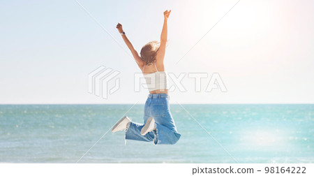 Happy woman, freedom and jump at beach with arms stretching for purpose, energy and motivation. Back view, success and fun at sea, summer vacation and sunshine travel, hope and wellness celebration 98164222